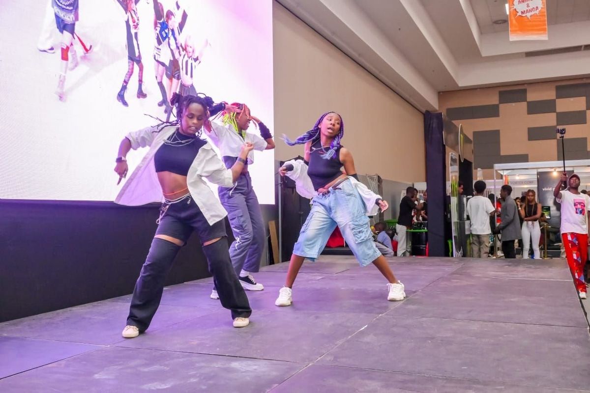 A group of dancers in K-Pop-inspired outfits performs on stage at the Nairobi Comic-Convention, featuring synchronized moves and energetic poses.