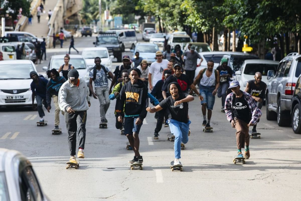 A group of skateboarders ride down a city street in Nairobi, surrounded by traffic and onlookers, capturing the energy and unity of the local skateboarding scene.