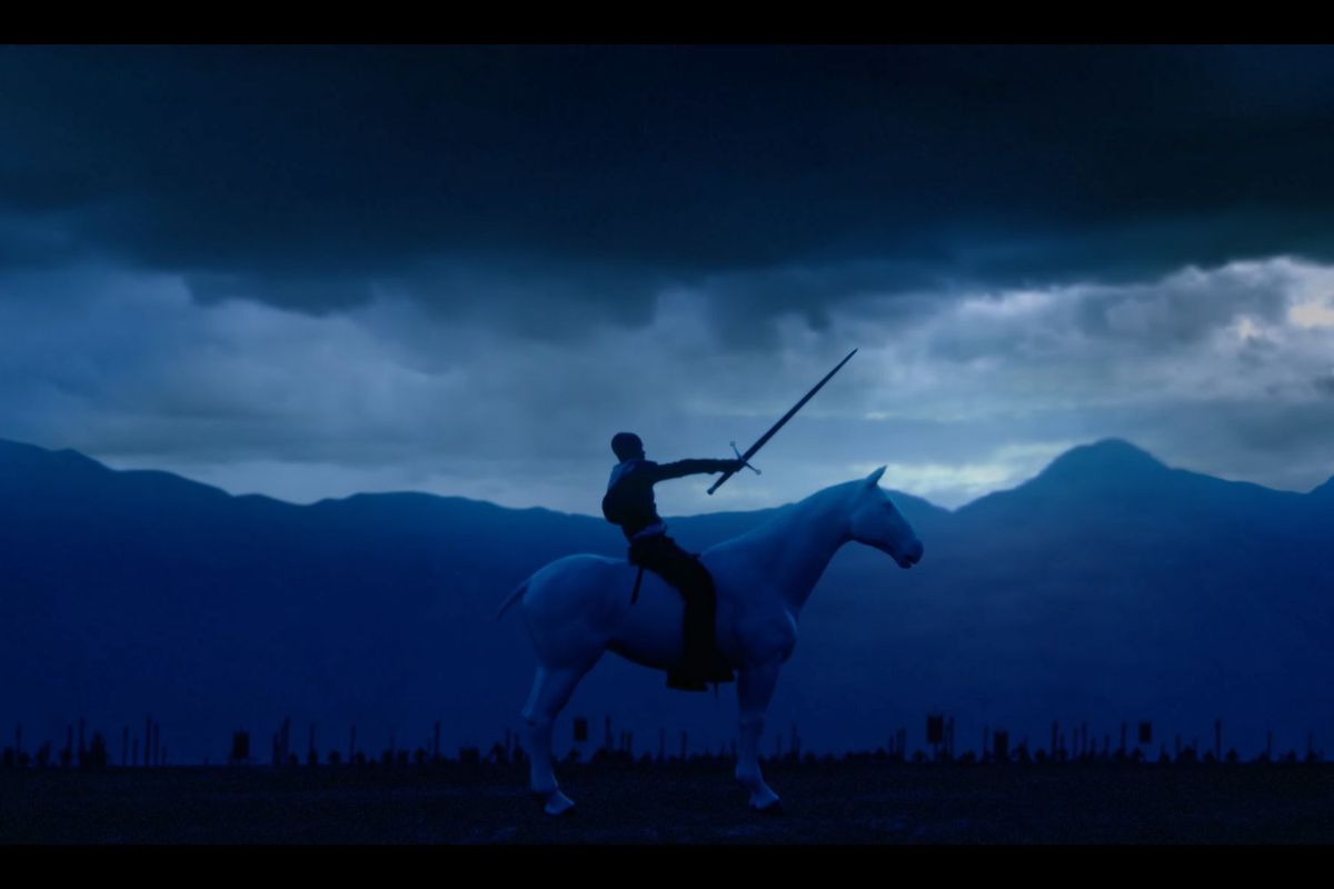 A lone person on a white horse raises a sword against a dramatic, stormy sky, set against a silhouette of mountains and distant flags