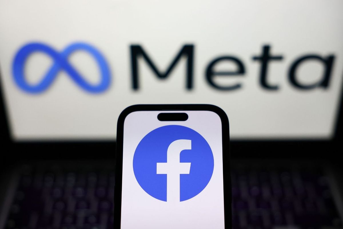 A smartphone displays the Facebook logo in front of a blurred screen showing the Meta logo, symbolizing Facebook’s parent company.