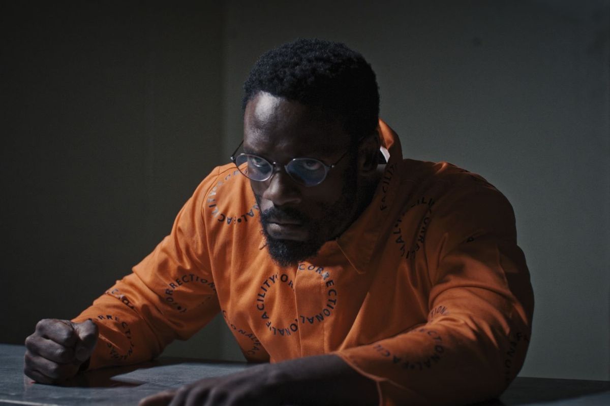 A still from ‘Red Ink,’ showing actor Bonko Khoza in an orange prison uniform slamming his fist on an interrogation table.