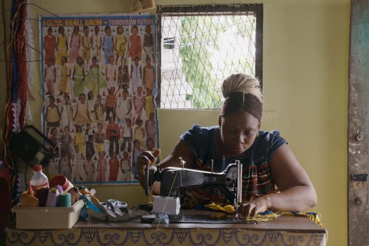 A still from the film, ‘Mambar Pierrette,’ of a woman sitting at a sewing machine.