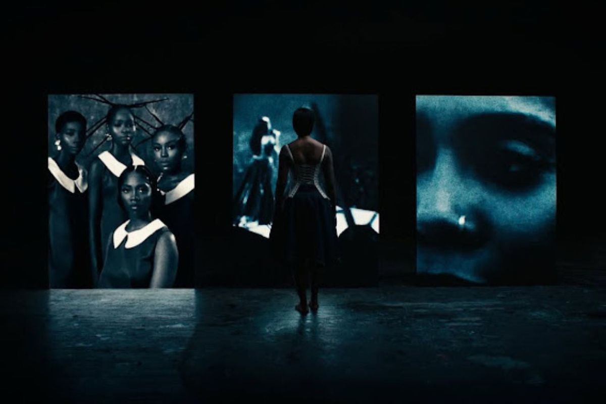 A woman stands in the shadow in front of three large screens.