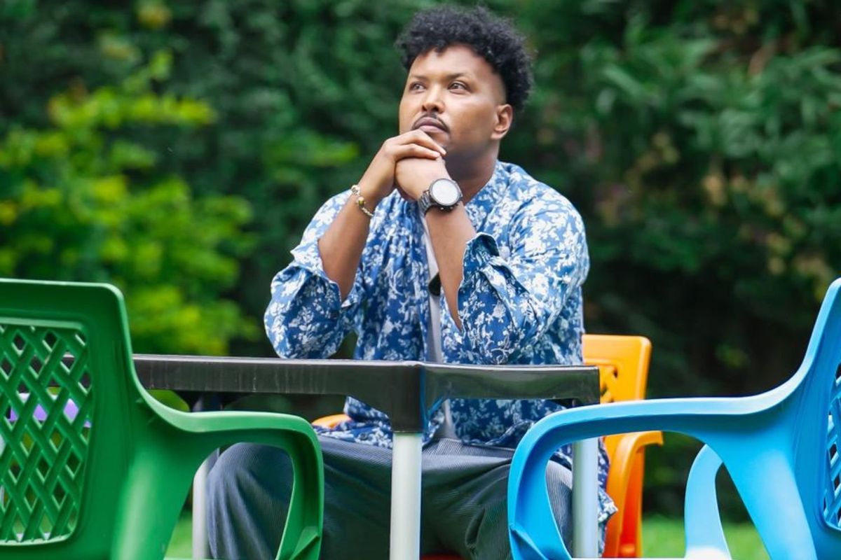Abdirizaq Hassan sits at an outdoor table surrounded by colorful plastic chairs, gazing into the distance. 