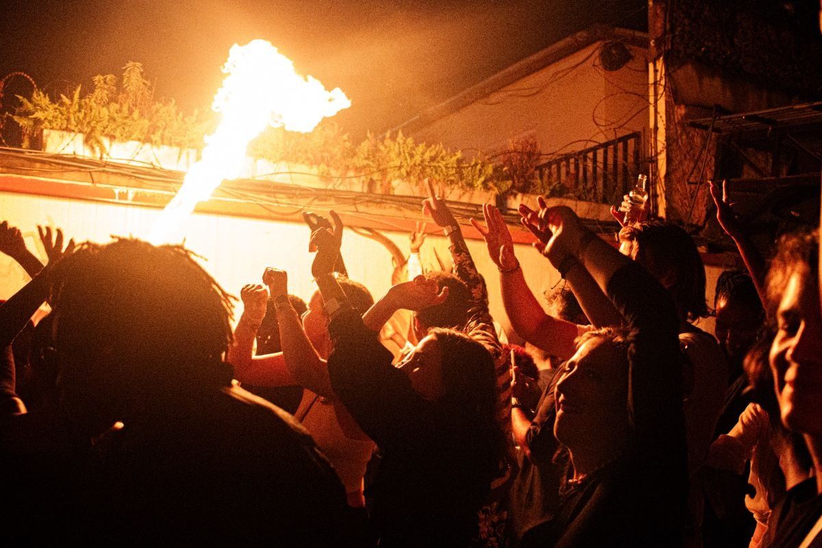 Fire is blown into the air and partygoers raise their hands during a rave.