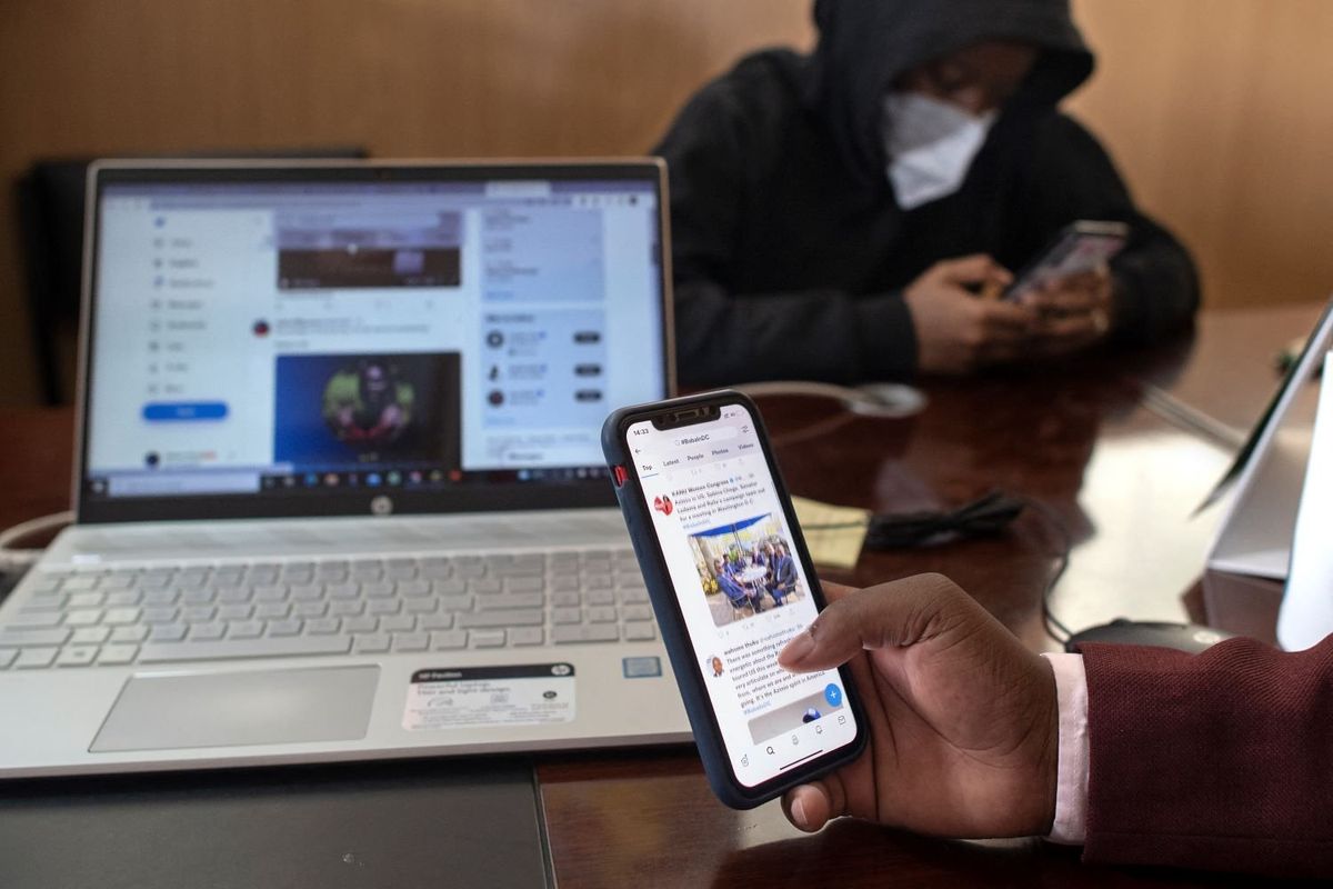 Ian James Mwai (R), 23, browses social media platforms on his mobile phone with a member of his outfit of social media influencers at an office in Thika town, central Kenya on April 26, 2022.