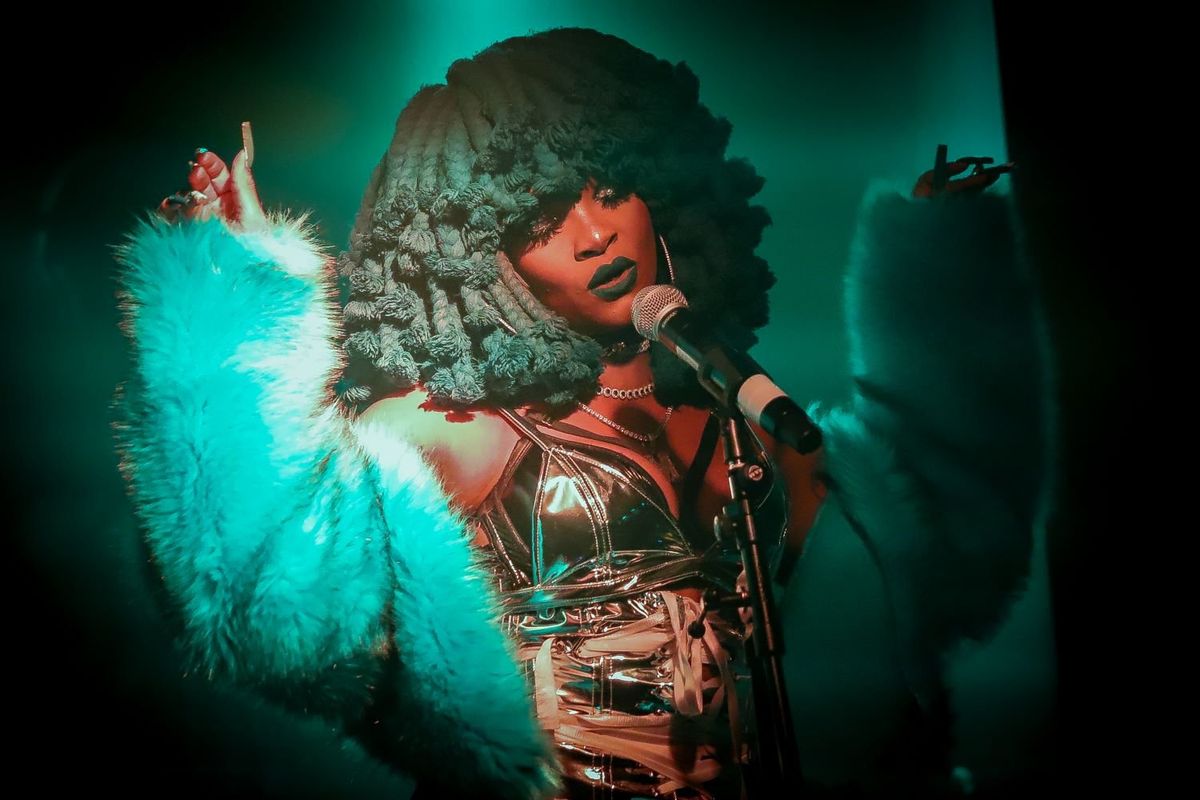 South African artist Moonchild Sanelly sings into a microphone as she’s bathed in a blue light.