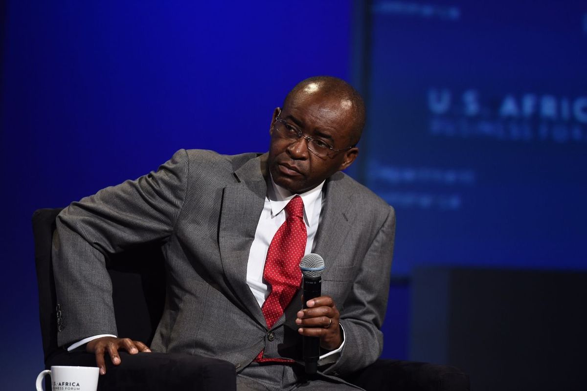 Strive Masiyiwa, sits on stage, wearing a grey suit and red tie, holding a microphone. He appears focused and thoughtful, with a cup labeled “U.S.-Africa Business Forum” placed in front of him. The background is lit in deep blue tones, creating a formal and professional atmosphere.
