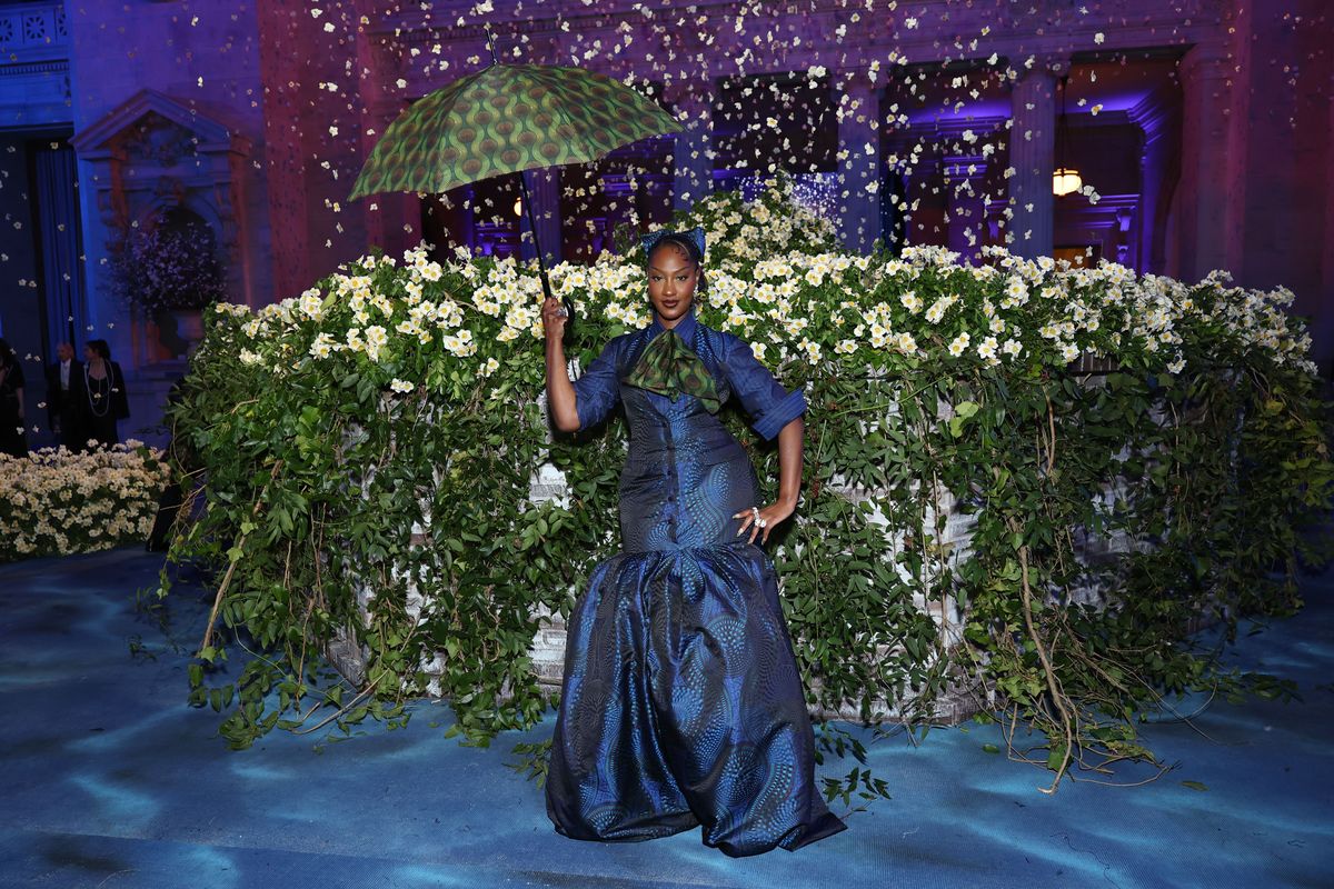 Tems in a blue Ankara suit dress with a puff skirt accented with a green cravat and a matching umbrella.