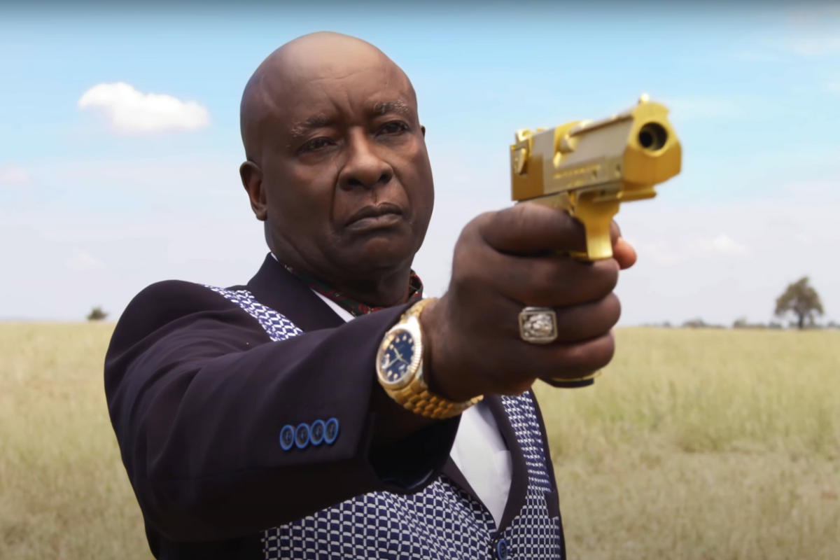 A man in a nice suite points a golden gun at the camera. 