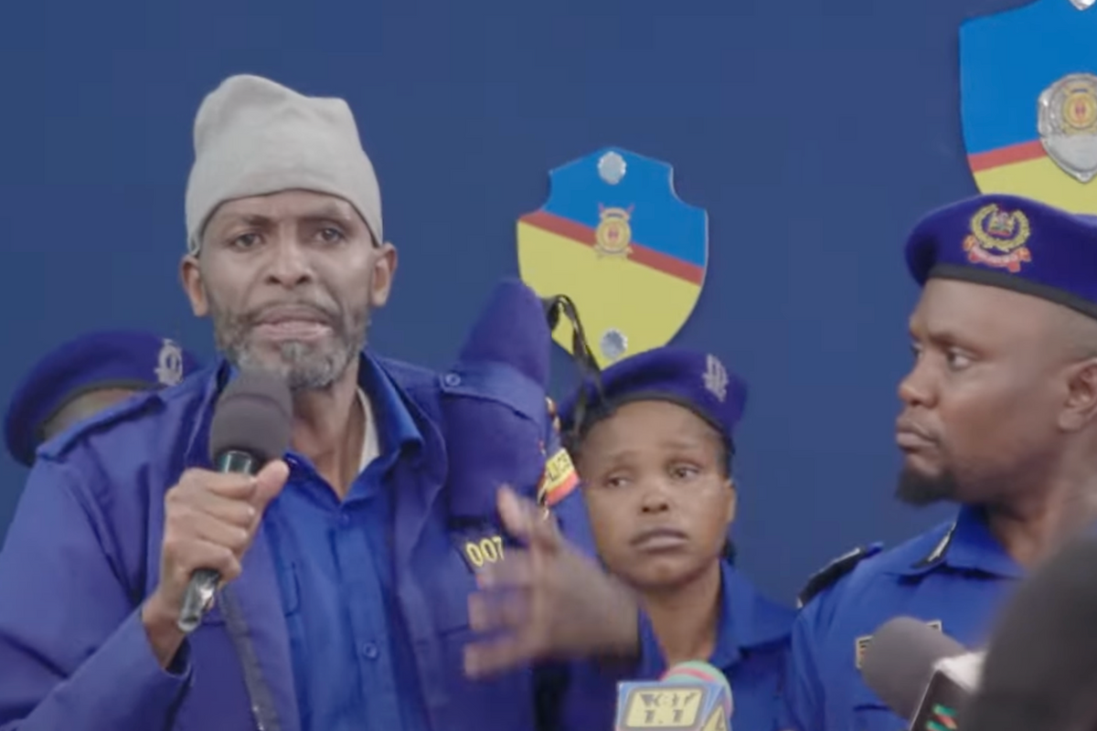 A still from 'Black & Blue Teaser Trailer' showing a man speaking with a microphone with about four people around him.