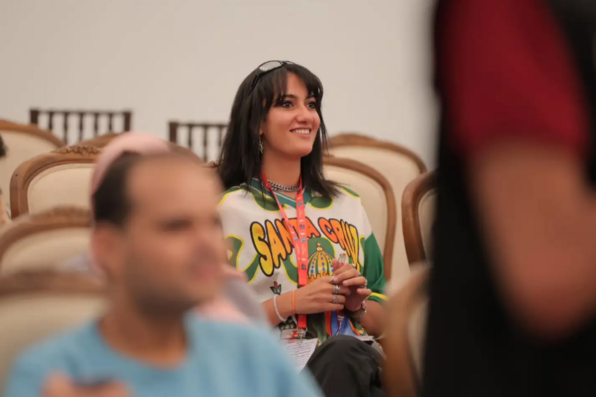 Menna Shanab wearing a green and white jersey, smiling in a conference room full of chairs.