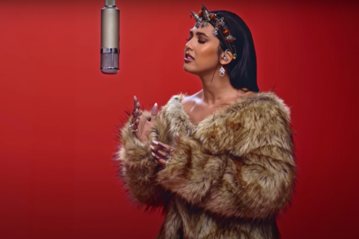 Moroccan pop singer Manal Benchlikha performs in a vegan fur coat in traditional Moroccan jewelry in front of a burgundy background at COLORSxSTUDIOS Berlin. 