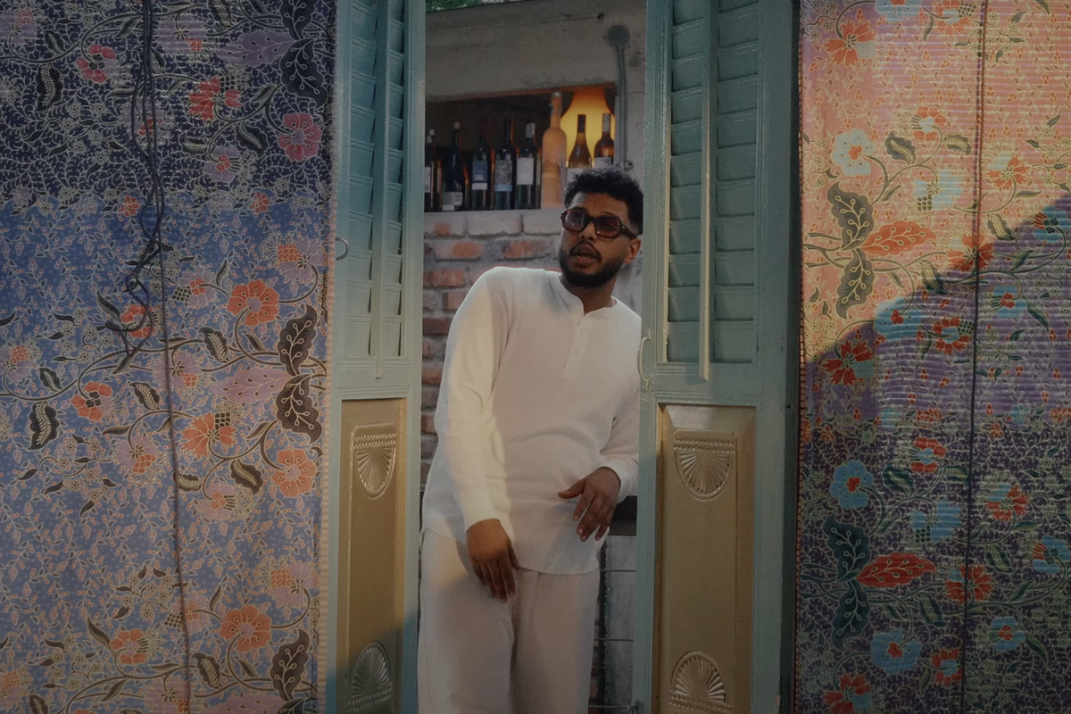 Soulja standing inside a green door frame, rapping. To his left and right are colorful walls with flower print. 